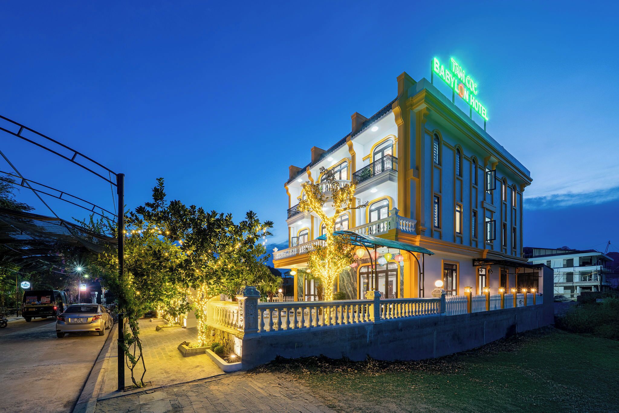 Een historisch pand met een neonbord waarop “Babylon Hotel” staat. Het heeft een klassieke architectuur met meerdere balkons en een goed verlichte gevel.
