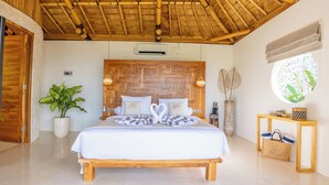 A bedroom with a wooden bed, a large potted plant, a wooden headboard, and a round mirror.