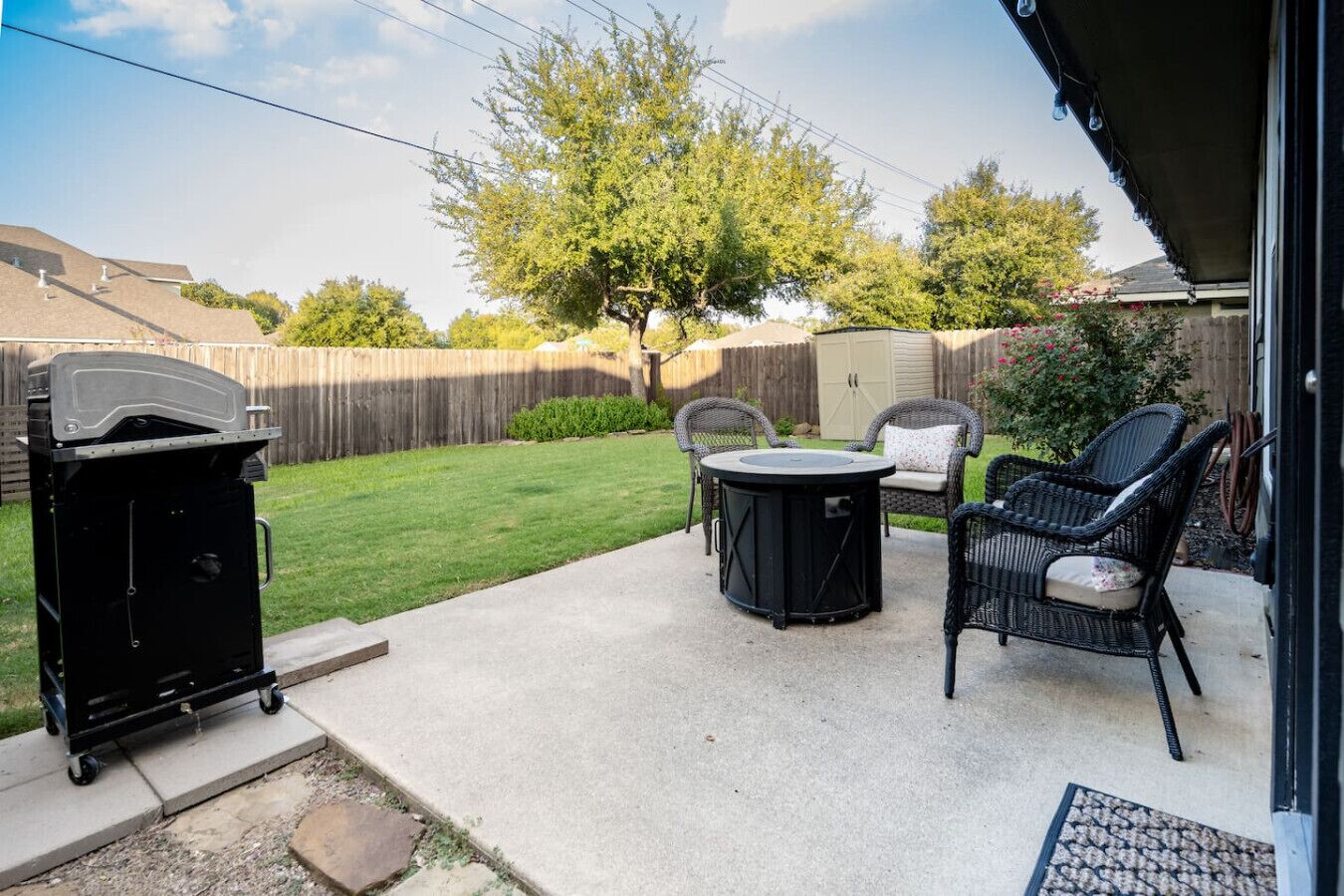 Eine Gartenpatio mit Grill, einem runden Tisch und zwei Korbstühlen.