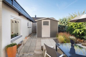 Eine Terrasse mit Tisch und Stühlen, ein kleines Gartenhaus und ein Fenster mit Herzdeko.
