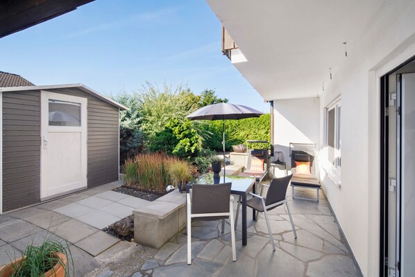 A patio with a table and chairs, a barbecue grill, and a shed.