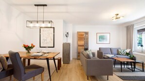 Una sala de estar moderna con comedor, sofás grises, una mesa de comedor de madera y una lámpara colgante.