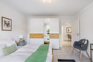 Ein Schlafzimmer mit Bett, Nachttisch, Stuhl, Kleiderschrank und einer Tür zu einem anderen Raum.