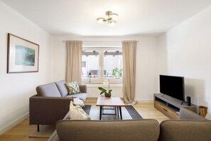 A living room with a sofa, a coffee table, a TV, and a window with curtains.