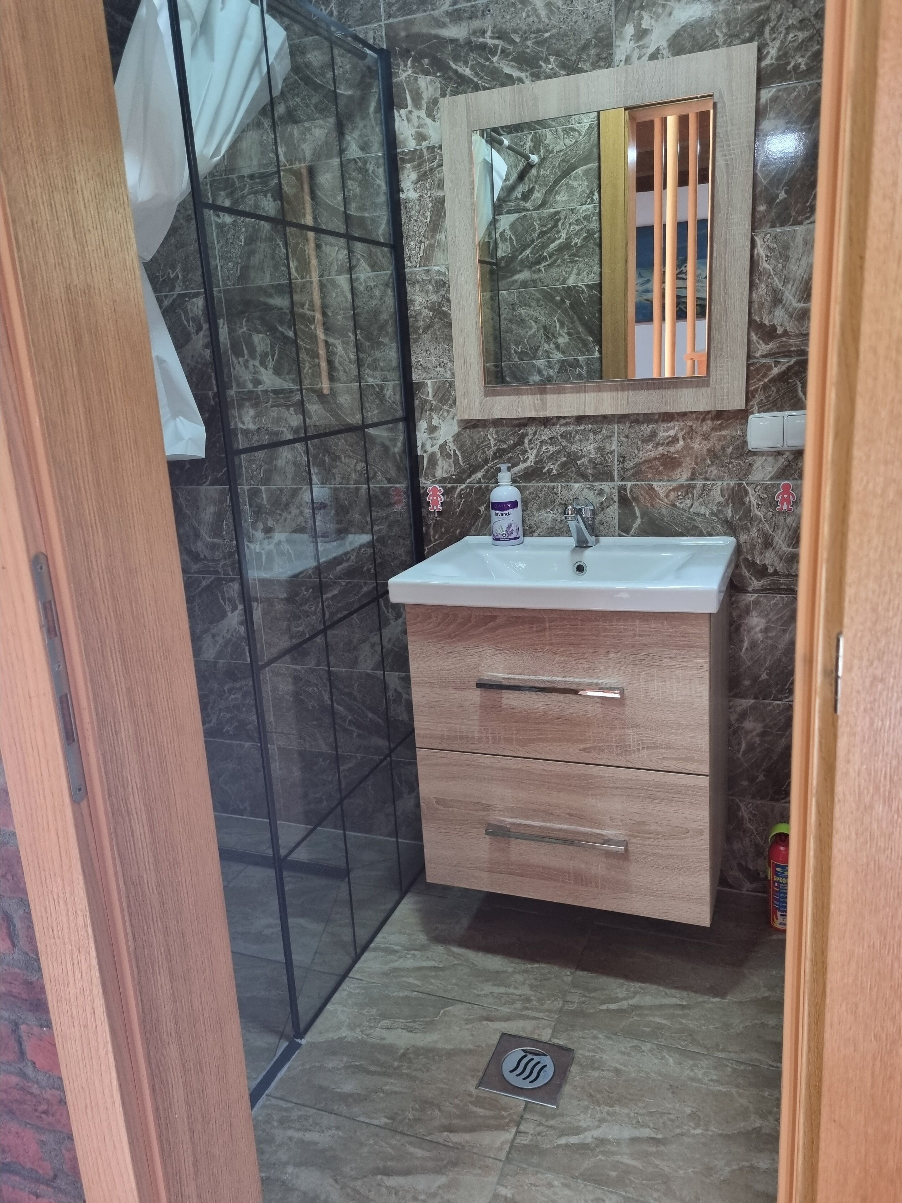 A bathroom with a marble-tiled wall, a wooden vanity with a mirror, and a shower enclosure.