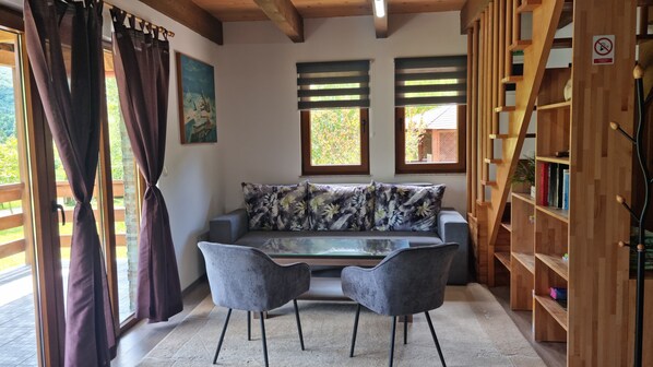 Ein gemütliches Zimmer mit einer Couch, zwei Sesseln, einem Holzregal und einem Bild an der Wand.