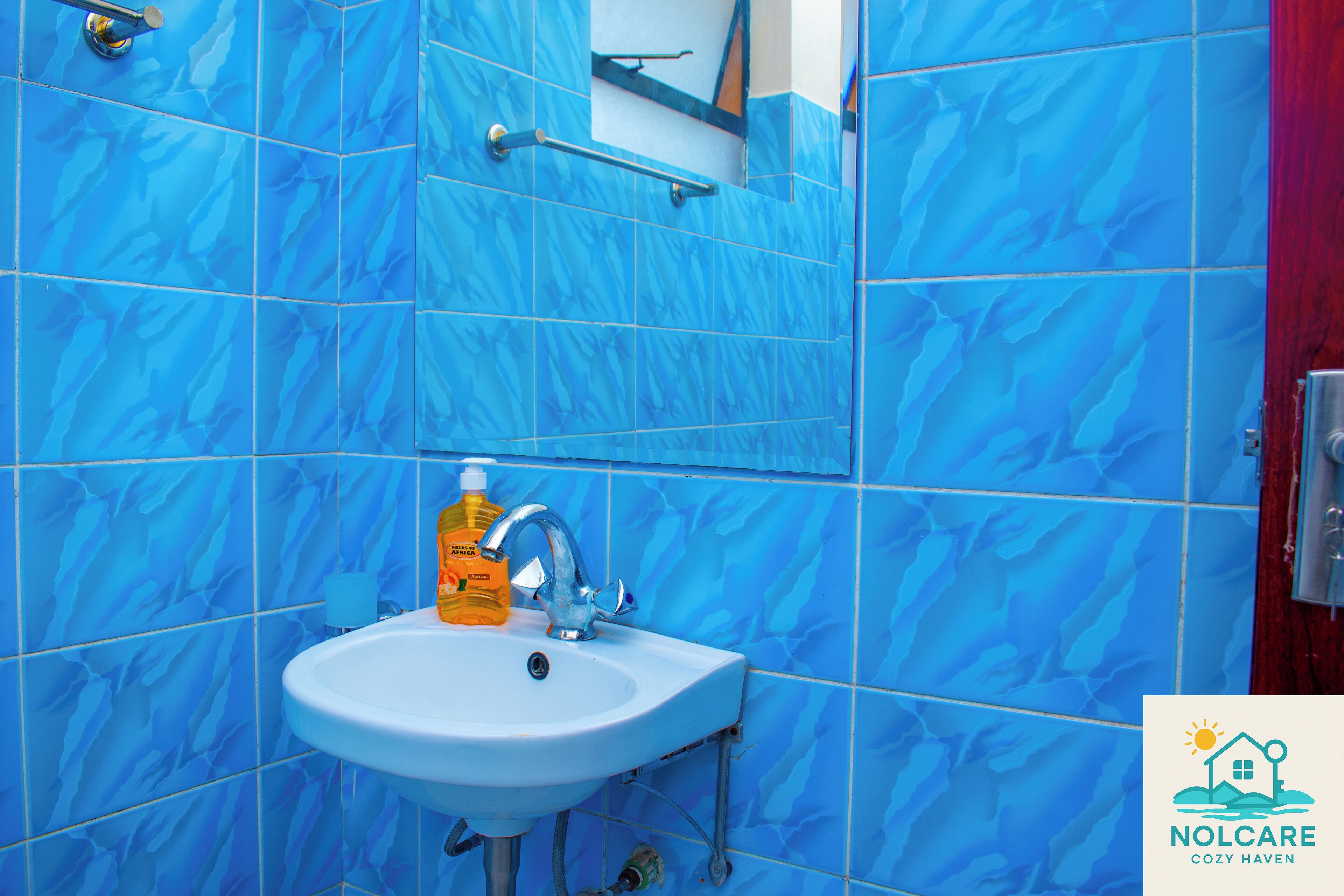 Een badkamer met blauwe marmeren tegels, een witte wastafel, een spiegel en een zeepdispenser.