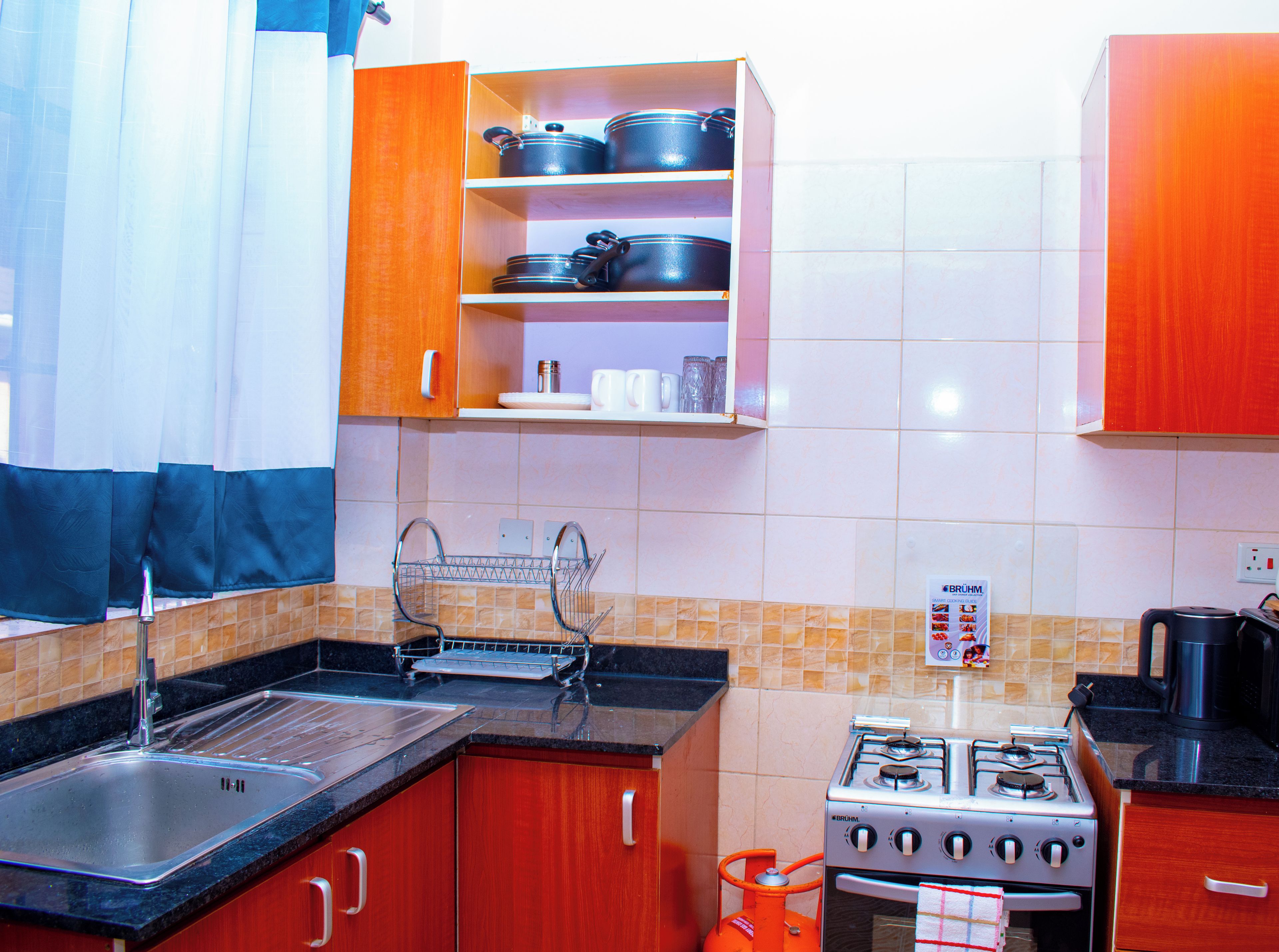 Een keuken met rode kastjes, een roestvrijstalen spoelbak, een gasfornuis en een magnetron.