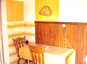 Een eetruimte met een houten tafel en stoelen, een klok aan de muur en een wandpaneel van hout.