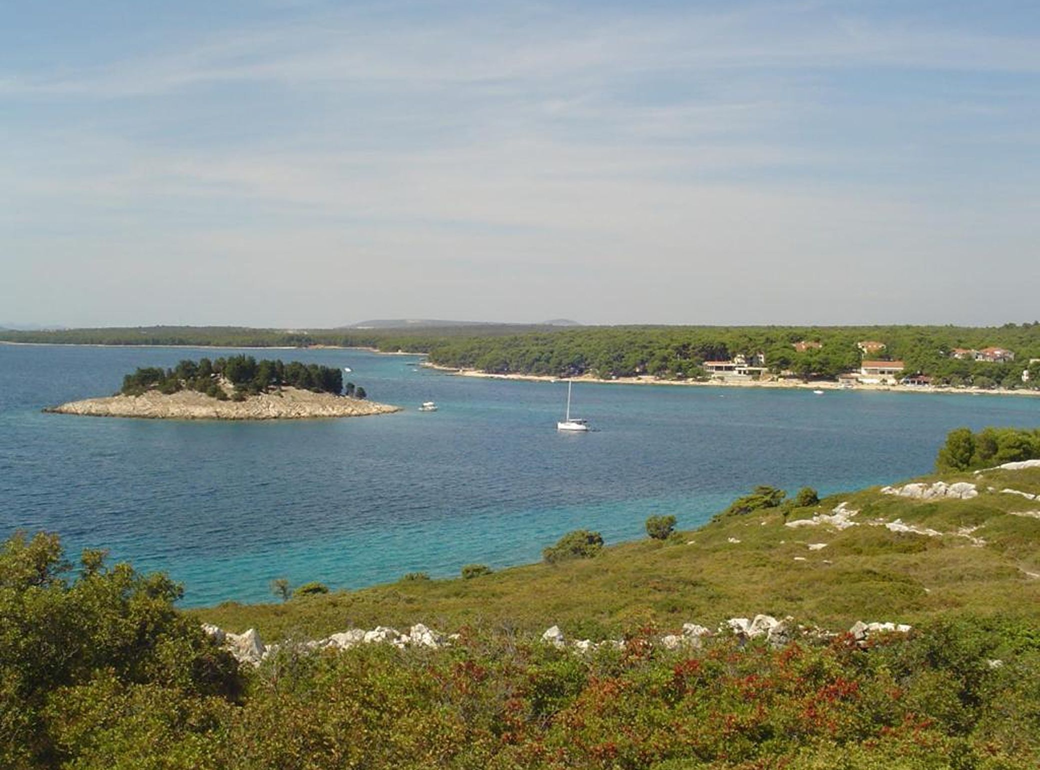 A coastal landscape with a small island, clear blue waters, and a sailboat.