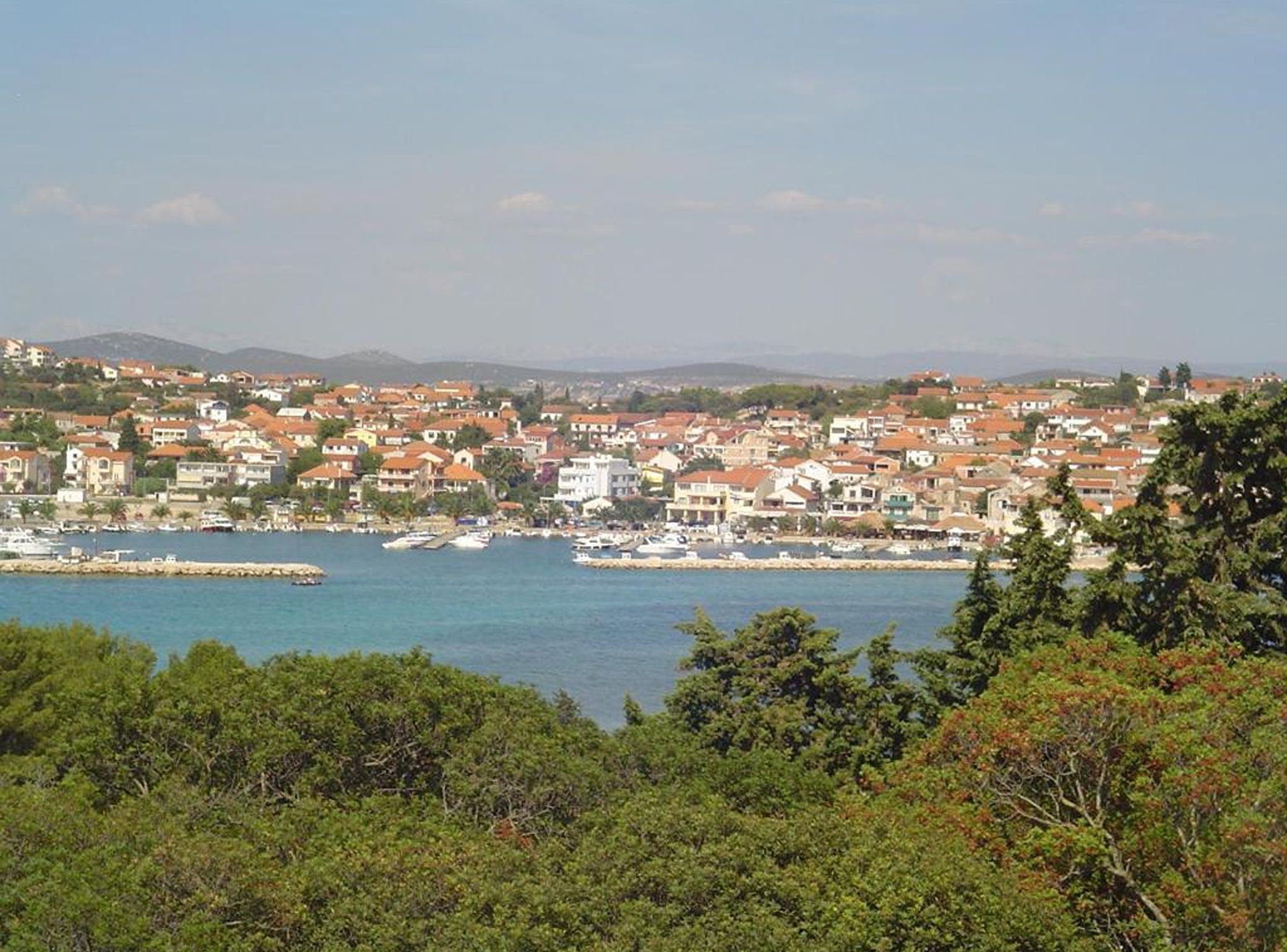 Un pueblo costero con viviendas densas, un puerto deportivo y una vista despejada del mar.