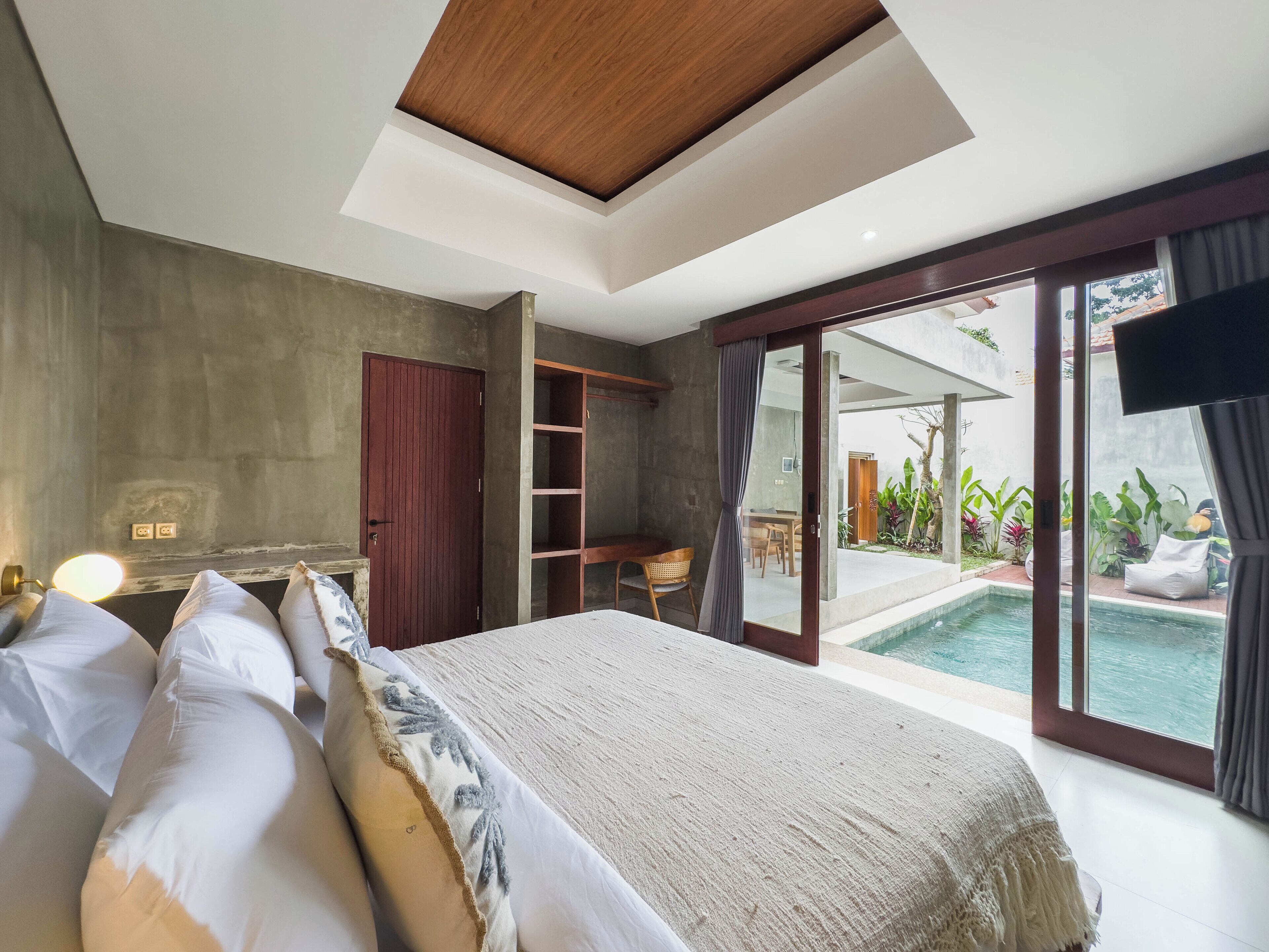 A bedroom with a large bed, a wardrobe, a desk, and a view of a swimming pool.