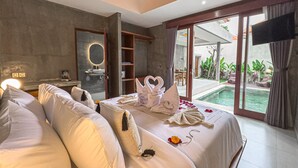 A modern hotel room with a large bed, a bathroom with a mirror, and a view of a pool. - Davaya Villas Ubud (Ubud)