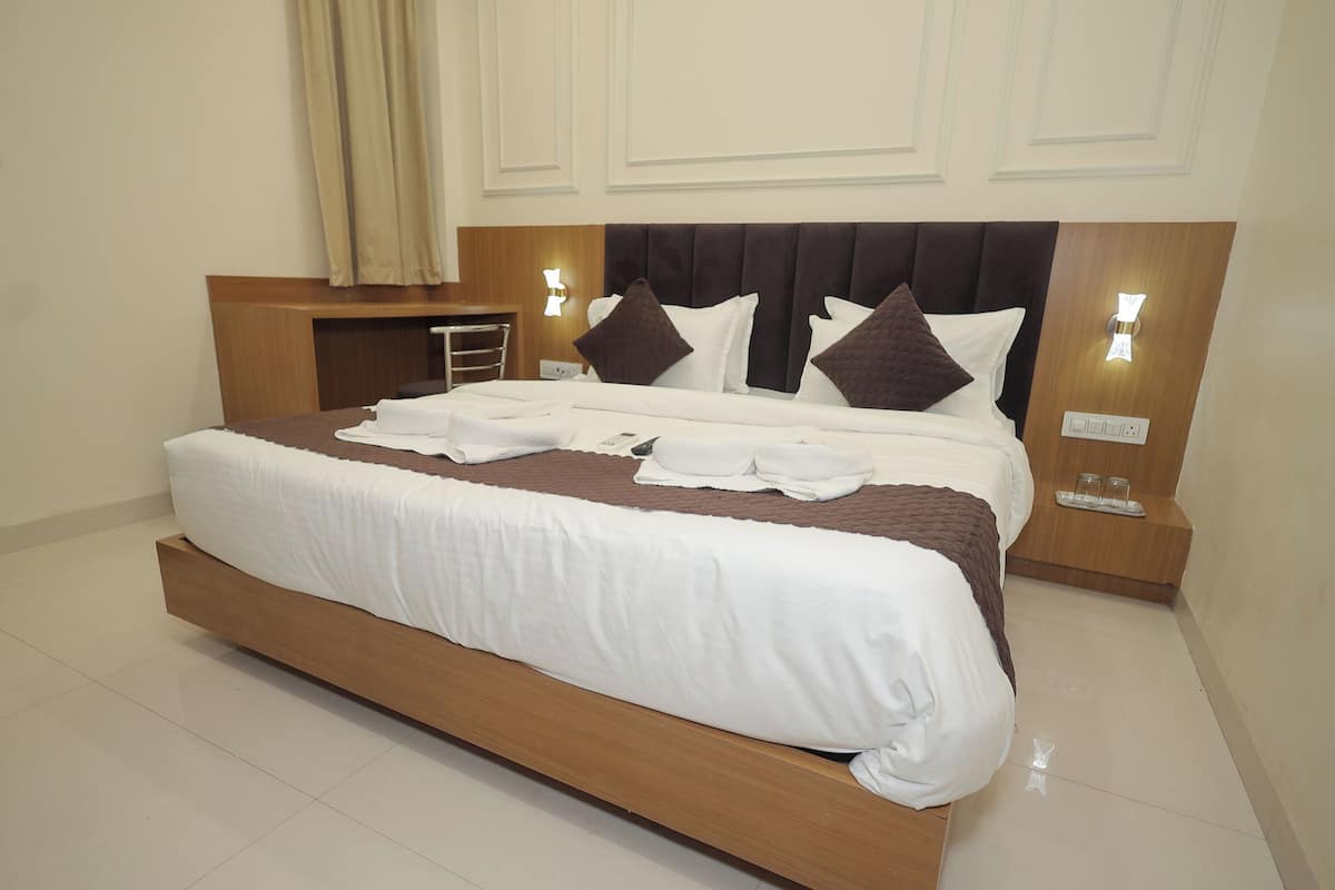 Una cama grande con estructura de madera, ropa de cama blanca y almohadas marrones. Hay dos mesitas de noche con lámparas y un pequeño estante con vasos.