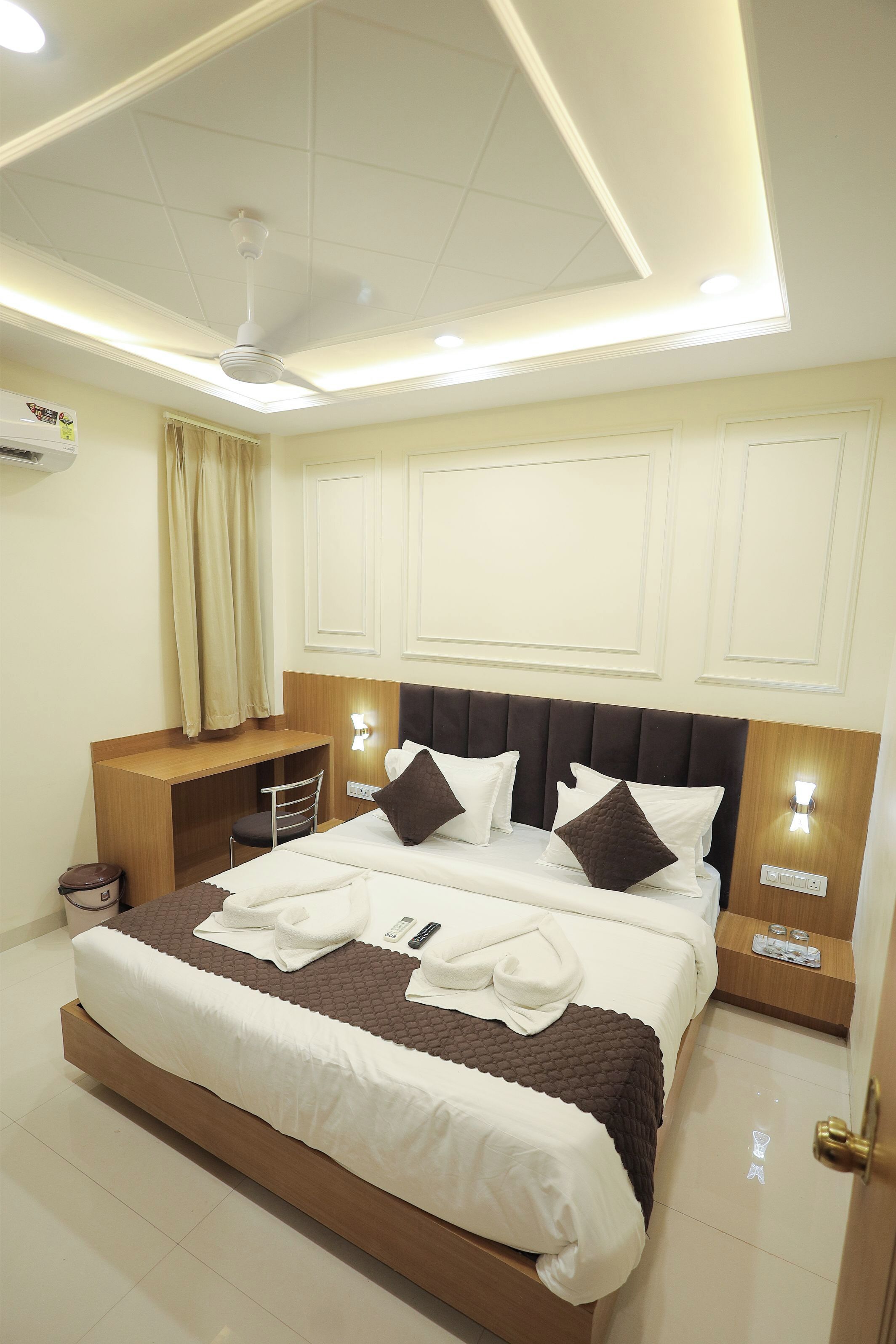 A hotel room with a large bed, a desk, a chair, a ceiling fan, and a nightstand with a lamp.