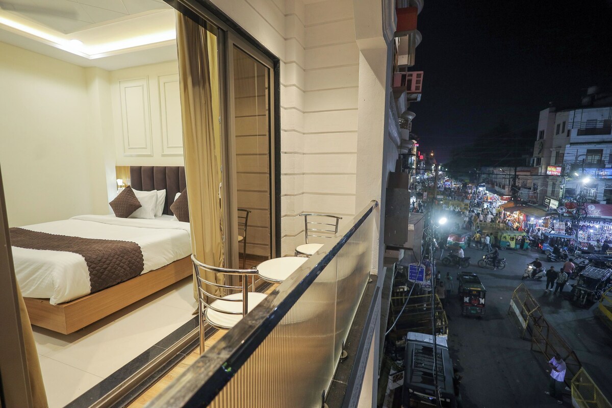 A hotel room with a bed, a chair, and a balcony overlooking a busy street at night.