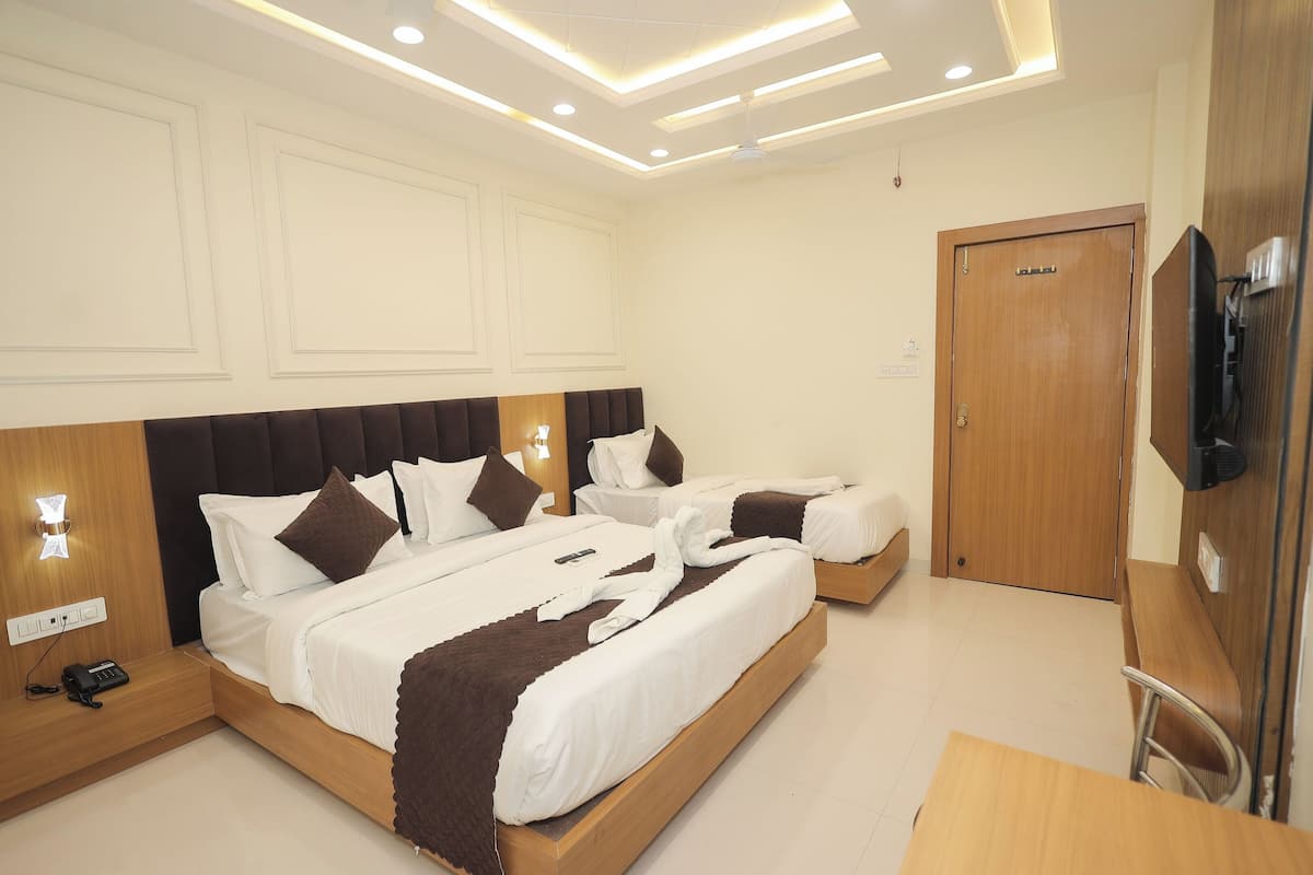 Una habitación de hotel con dos camas, cabecero de madera, mesita de noche con un teléfono y televisor montado en la pared.