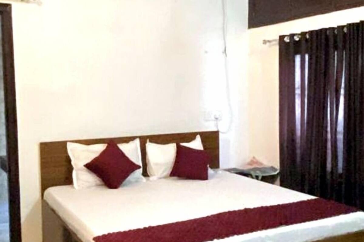 Una cama individual con estructura de madera, ropa de cama blanca y dos almohadas rojas. Una unidad de aire acondicionado está montada en la pared sobre la cama.
