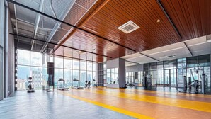 Ein großzügiger Fitnessraum mit Trainingsgeräten, großen Fenstern und hoher Decke.