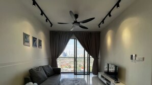 Ein modernes Wohnzimmer mit einem grauen Sofa, einem flauschigen Teppich, einem Deckenventilator und einem Fernseher auf einem weißen Schrank.