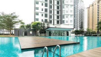 A swimming pool with a wooden deck and metal railings, surrounded by modern high-rise buildings.