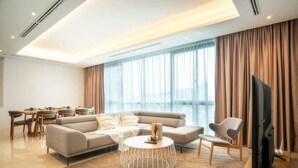 Ein modernes Wohnzimmer mit Sofa, Couchtisch, Fernseher und großen Fenstern mit Vorhängen.