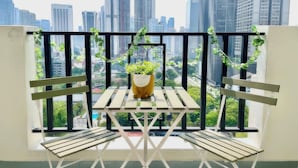 A balcony with a wooden table and chairs, a potted plant, and a view of a cityscape with tall buildings. - The Embassy Row 206 Apartments (Kuala Lumpur)