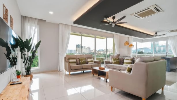 A modern living room with a sofa, armchair, and coffee table, large windows with a city view, and a ceiling fan. - The Embassy Row 206 Apartments (Kuala Lumpur)