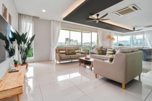 A modern living room with a sofa, armchair, and coffee table, large windows with a city view, and a ceiling fan. - The Embassy Row 206 Apartments (Kuala Lumpur)