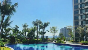 A swimming pool with a tiled edge and lounge chairs, surrounded by palm trees and a high-rise building in the background. - Aradia Residence Lake City KL North (Kuala Lumpur)
