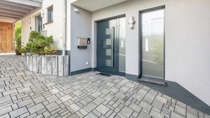 A modern building entrance with a paved walkway, a dark-colored door, and a small potted plant.