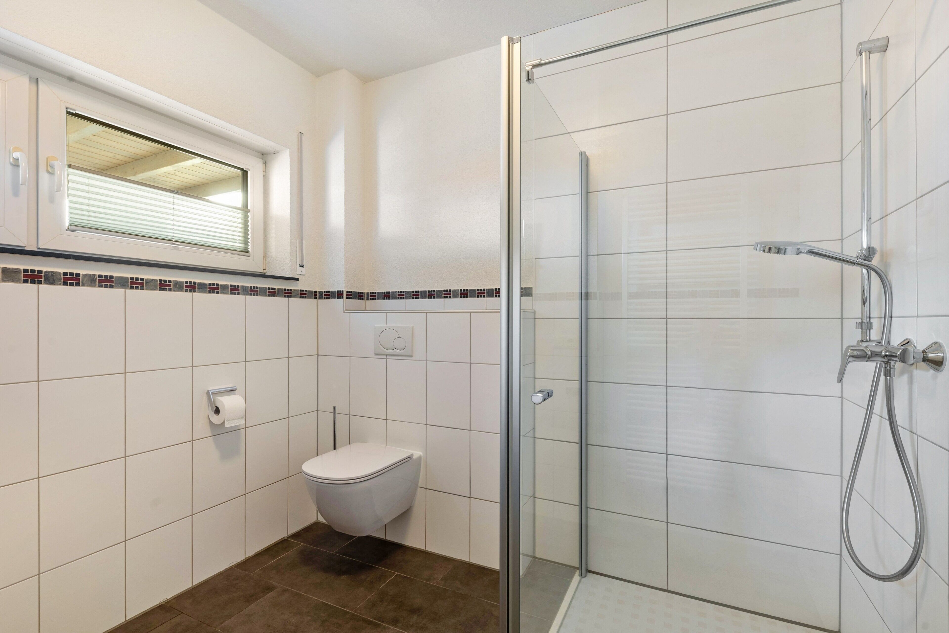 Une salle de bain comprenant des toilettes, une douche avec une porte en verre et une fenêtre avec des stores.
