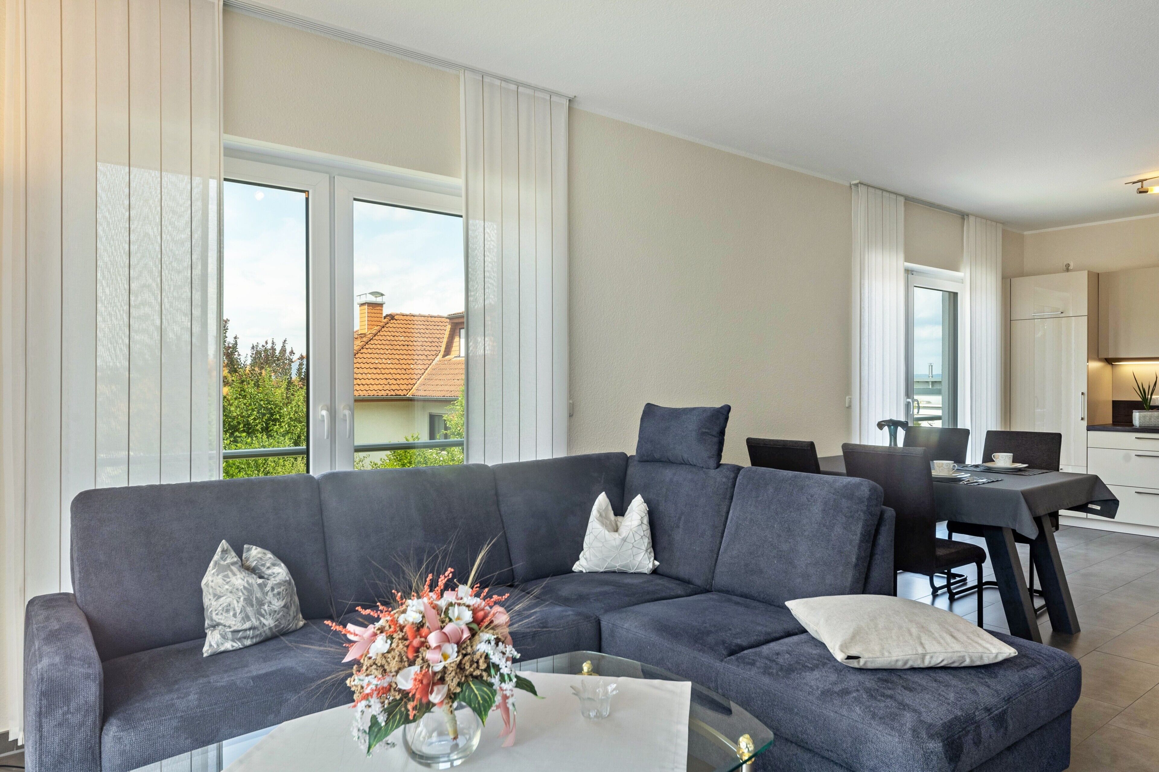 Ett modernt vardagsrum med en grå soffa, ett soffbord i glas och en matplats med ett bord och stolar.