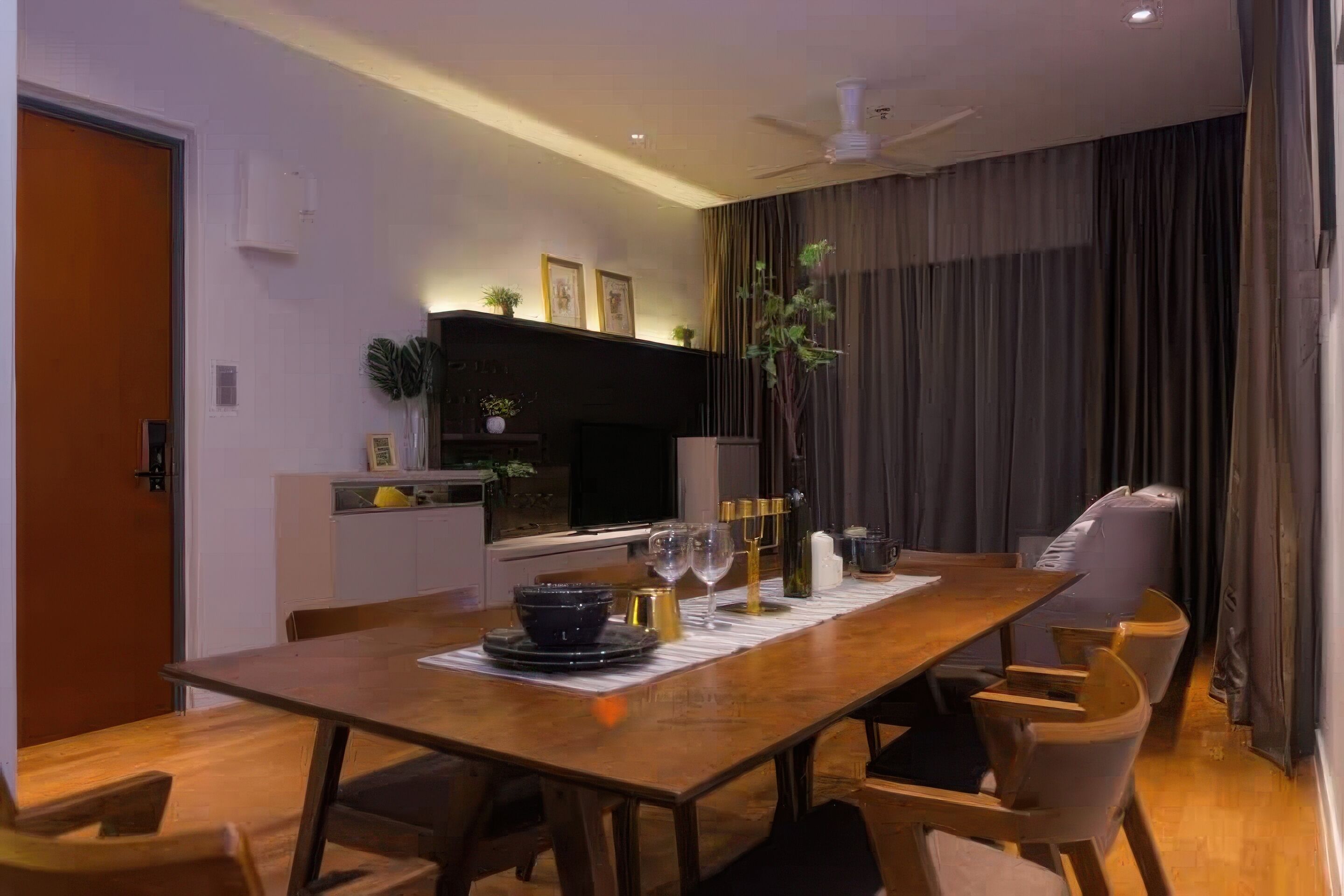 A modern dining area with a wooden table set for two, a kitchen in the background, and a ceiling fan.