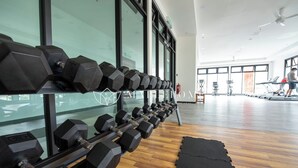 Ein Fitnessraum mit einer Reihe sechseckiger Kurzhanteln auf einem Gestell, Holzboden und großen Fenstern.