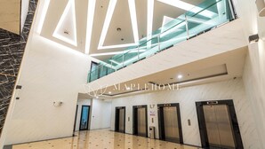Eine geräumige Lobby mit hoher Decke, Marmorböden und einer gläsernen Treppe, die in eine obere Etage führt.