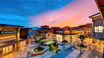 A shopping mall with a Coach store, surrounded by palm trees and illuminated by sunset.