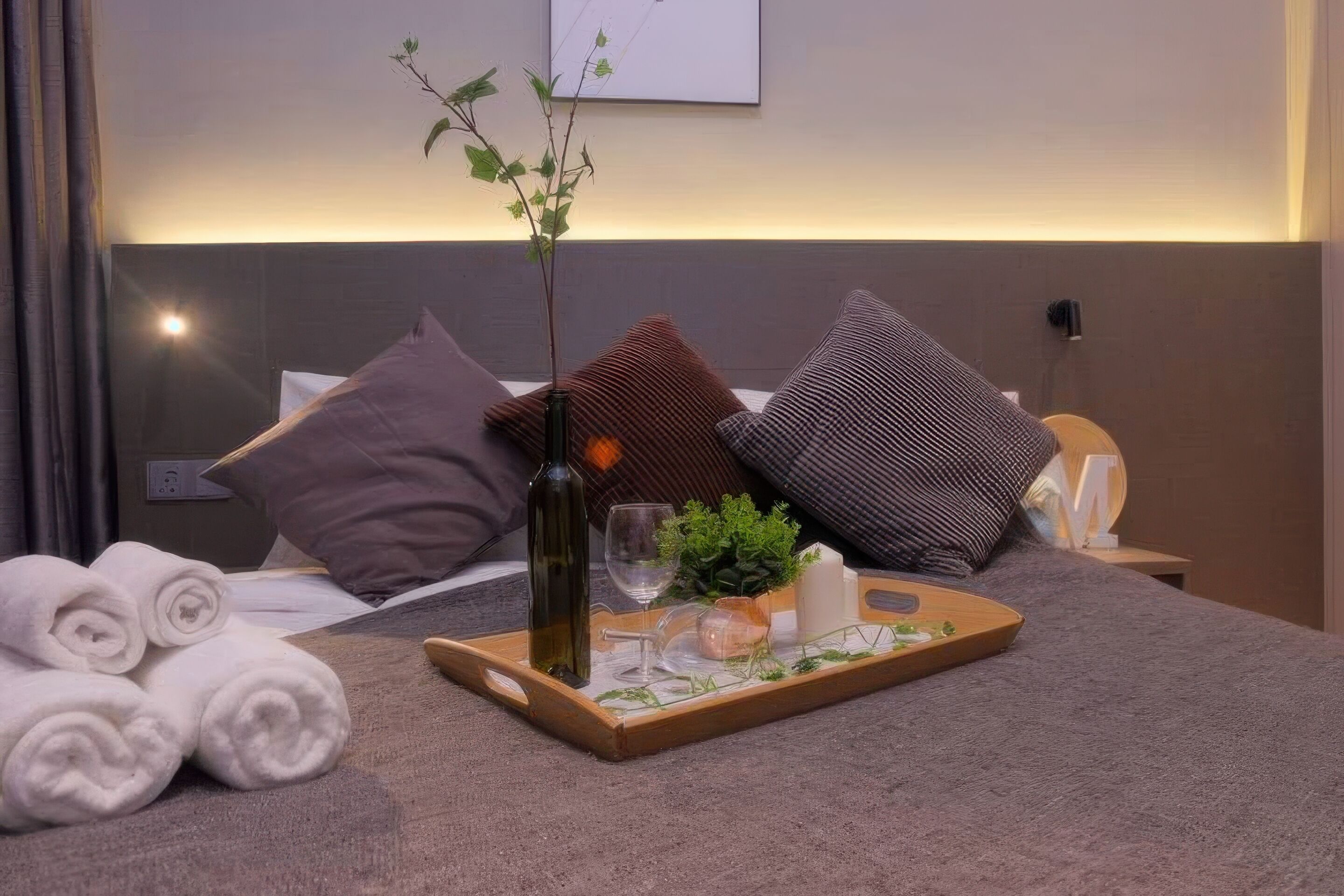 Ein ordentlich bezogenes Bett mit aufgerollten weißen Handtüchern, ein Tablett mit einer Flasche, Gläsern und einer Pflanze.