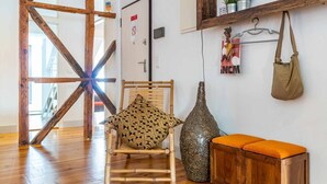 A room with a wooden floor, a chair with a patterned cushion, a decorative vase, and a wooden cabinet with an orange cushion. - Stylish 2BR Loft w/ Views • Av. Liberdade & Metro (Lisbon)