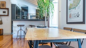 A modern kitchen with a large wooden table, bar stools, and a potted plant. - Stylish 2BR Loft w/ Views • Av. Liberdade & Metro (Lisbon)