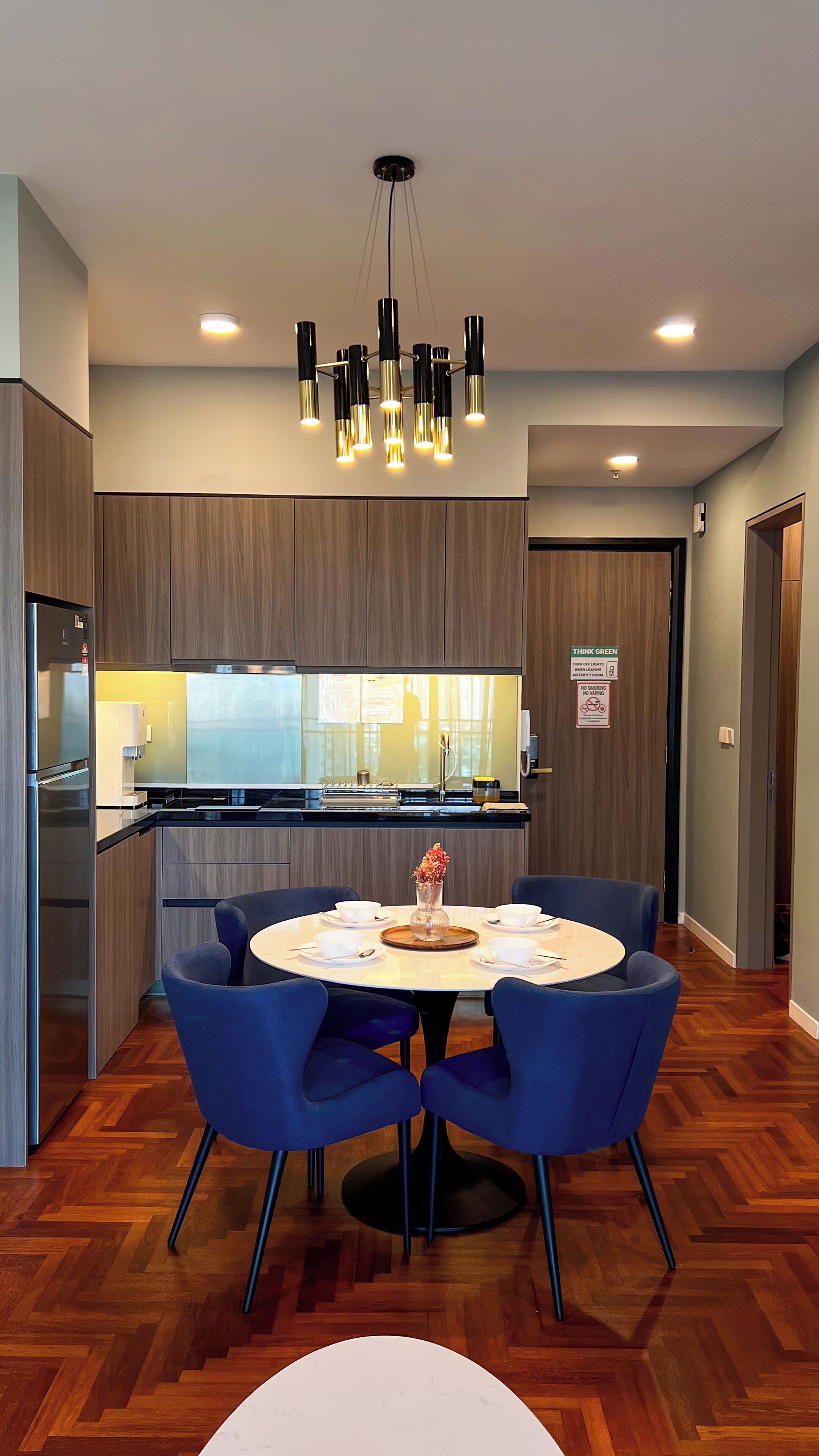 A modern kitchen with a central island, a dining area with blue chairs, and a chandelier.