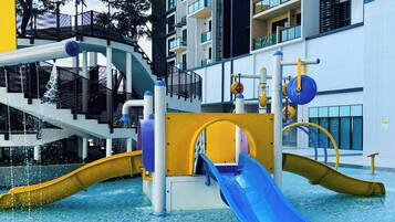 A water park with slides and water features, surrounded by a high-rise building.