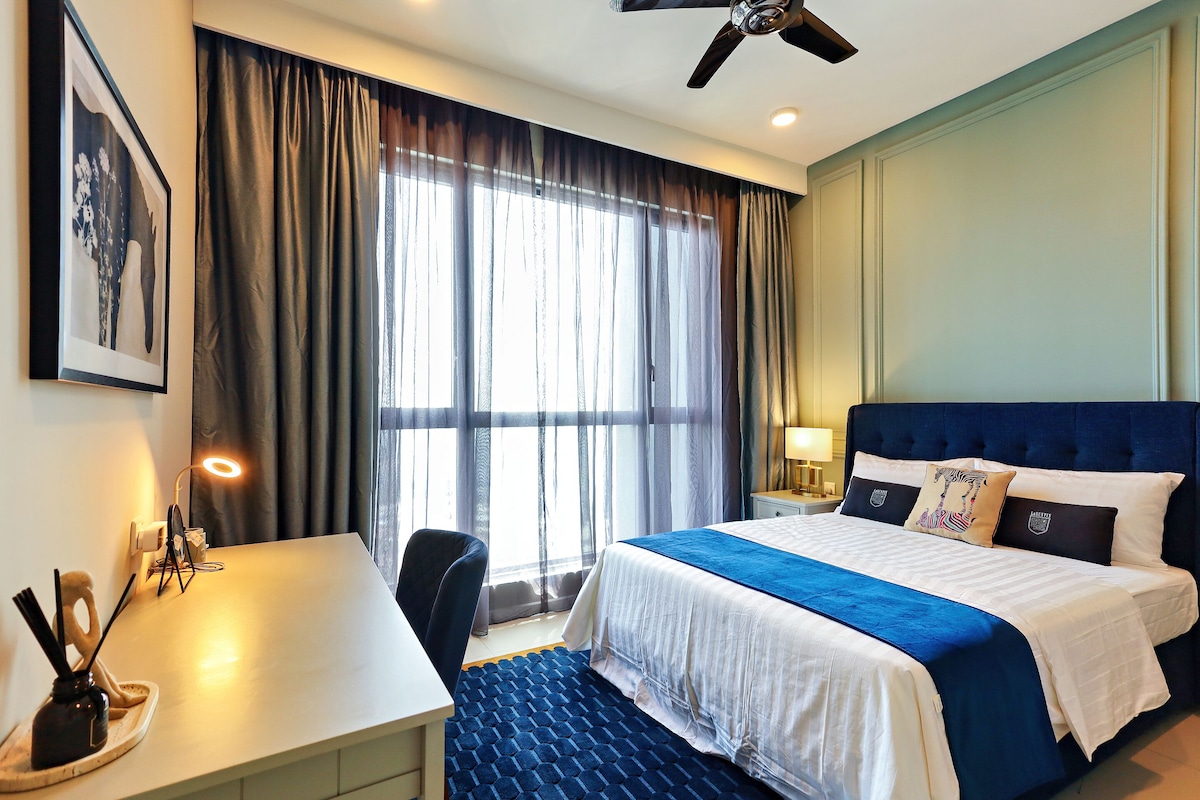 A hotel room with a bed, desk, chair, and a large window with curtains.