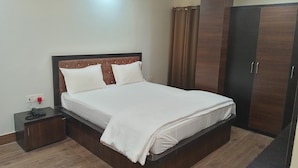 Een opgemaakt bed met een houten hoofdbord, een nachtkastje met een telefoon, en een kledingkast met een spiegel.