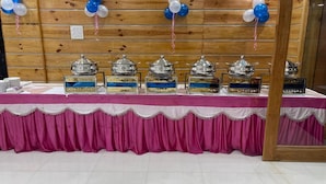 Een feesttafel met een roze tafelkleed, zilveren servies en blauw-witte ballonnen.