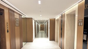 A modern hotel corridor with wooden paneling, numbered doors, and a digital elevator display.