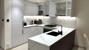 A modern kitchen with white cabinetry, a marble countertop, and a built-in sink.