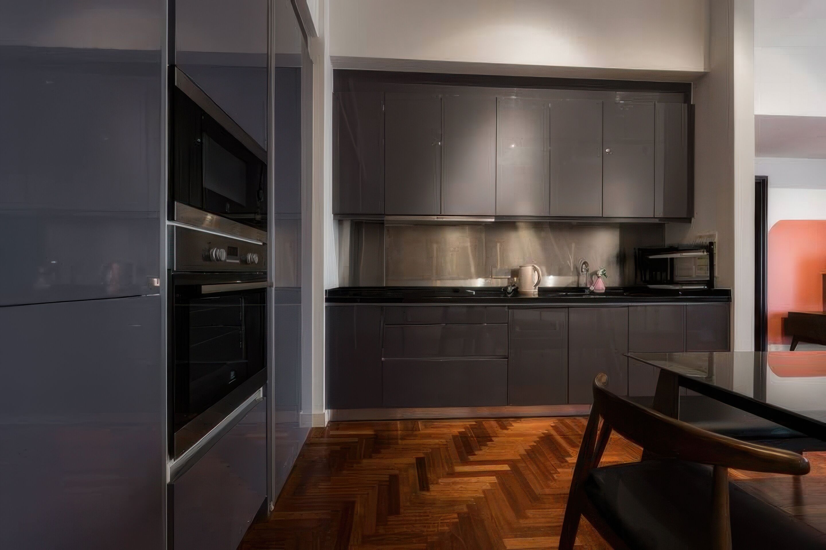 Una cucina moderna con mobili scuri, un forno a microonde e un pavimento in legno a spina di pesce.