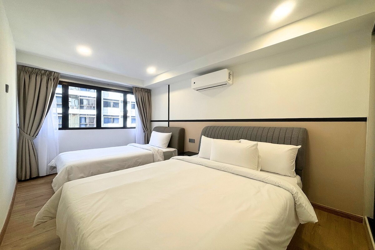 Une chambre d’hôtel avec deux lits, une fenêtre avec des rideaux, un appareil de climatisation et une vue sur les bâtiments environnants.