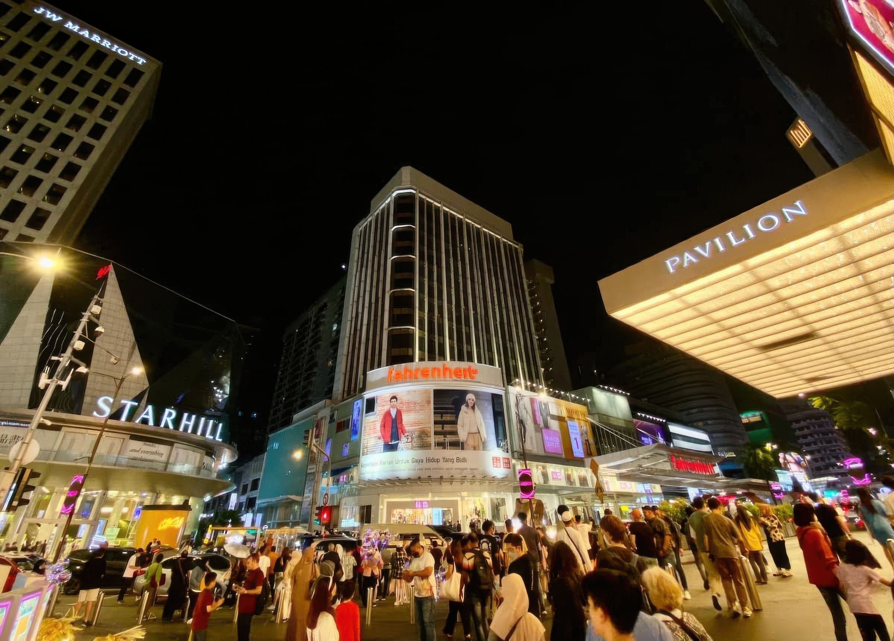A busy urban street scene with a prominent building featuring a large sign for 'Starhill' and 'Pavilion'.